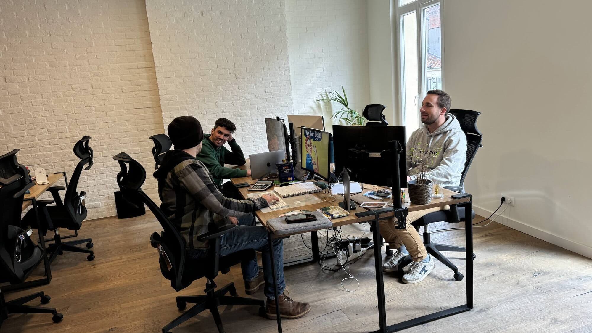 Three people working at their desks in an open space with whitewashed brick walls